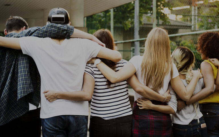 Smiling happy young adult friends arms around shoulder outdoors friendship and connection concept
